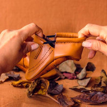 Load image into Gallery viewer, hands pulling Soft Sole leather flexible handmade baby and toddler shoes moccs moccasins made in Peru genuine leather wide foot barefoot like shoes slip on feet sandal spring summer brown caramel neutral unisex