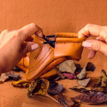 Load image into Gallery viewer, hands pulling Soft Sole leather flexible handmade baby and toddler shoes moccs moccasins made in Peru genuine leather wide foot barefoot like shoes slip on feet sandal spring summer brown caramel neutral unisex