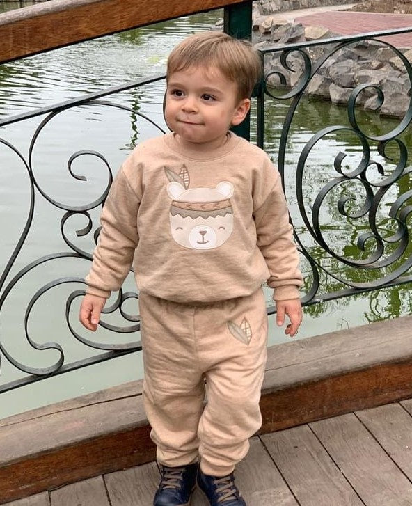 organic cotton undyed and raw. Brown, neutral and  beige color. Two piece sweatshirt and sweat pants set with bear applique. Boy standing on bridge.
